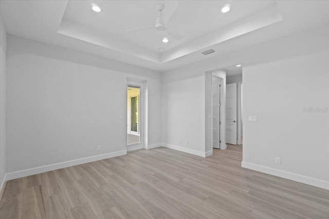 spare room featuring light wood finished floors, ceiling fan, baseboards, and a raised ceiling