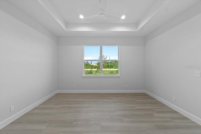 unfurnished room with light wood finished floors, baseboards, a tray ceiling, and recessed lighting