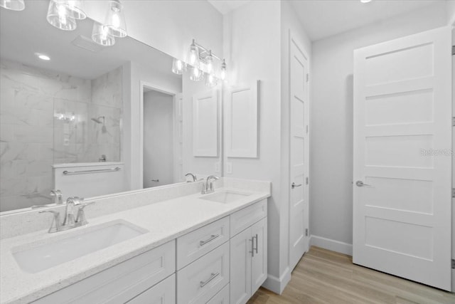 full bath featuring a tile shower, double vanity, wood finished floors, and a sink