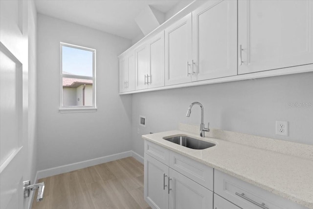 laundry room with cabinet space, baseboards, light wood-type flooring, washer hookup, and a sink