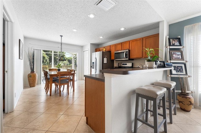 kitchen featuring a breakfast bar, stainless steel appliances, dark countertops, hanging light fixtures, and brown cabinetry