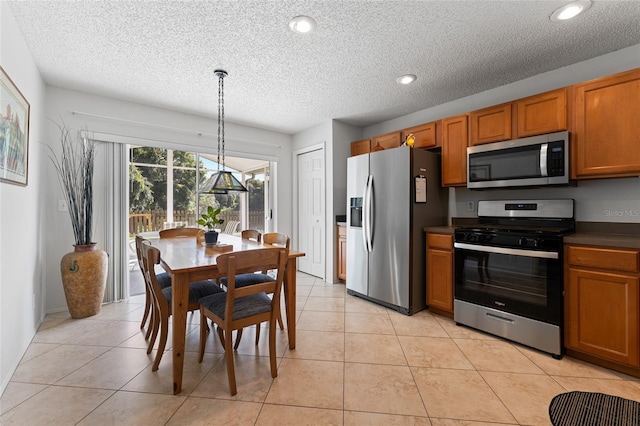 kitchen featuring light tile patterned flooring, stainless steel appliances, brown cabinetry, dark countertops, and decorative light fixtures