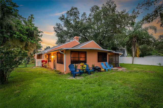 back house at dusk featuring a lawn