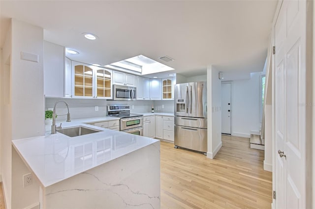 kitchen with white cabinets, backsplash, light wood-type flooring, stainless steel appliances, and sink