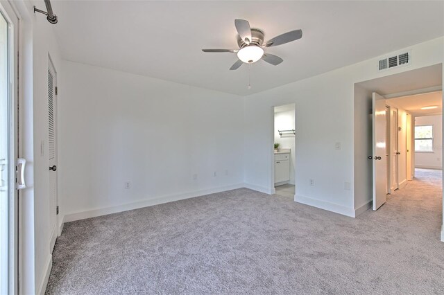 unfurnished bedroom with light carpet, baseboards, visible vents, a ceiling fan, and ensuite bathroom