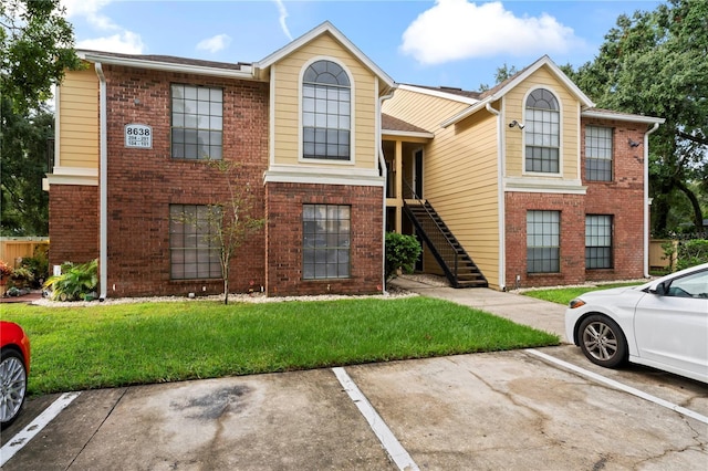 view of front of property with uncovered parking, brick siding, stairway, and a front lawn