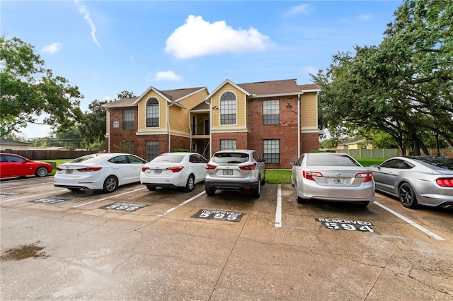 view of front of home with uncovered parking, brick siding, and fence