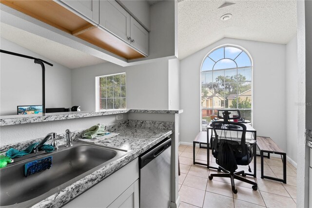 kitchen with light tile patterned floors, a textured ceiling, a sink, vaulted ceiling, and dishwasher