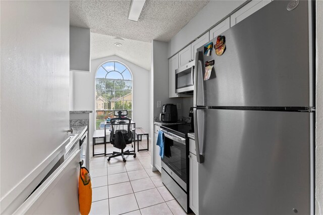 kitchen with light tile patterned floors, stainless steel appliances, white cabinetry, vaulted ceiling, and a textured ceiling