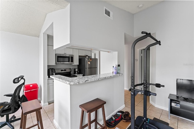 kitchen featuring light tile patterned floors, visible vents, baseboards, appliances with stainless steel finishes, and a peninsula