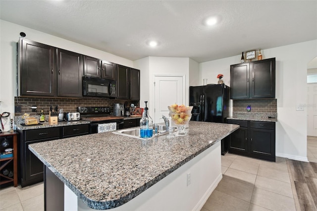 kitchen with black appliances, a center island with sink, a sink, light tile patterned floors, and decorative backsplash