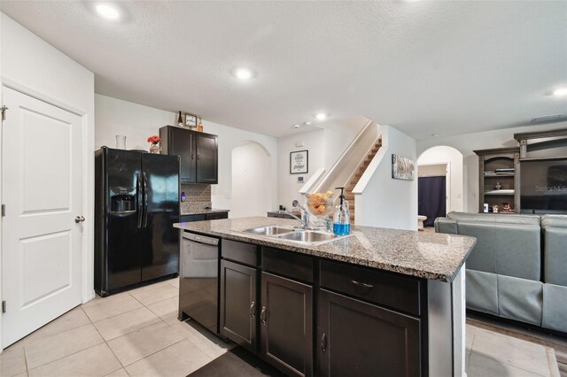 kitchen with black refrigerator with ice dispenser, dishwasher, sink, an island with sink, and light tile patterned floors