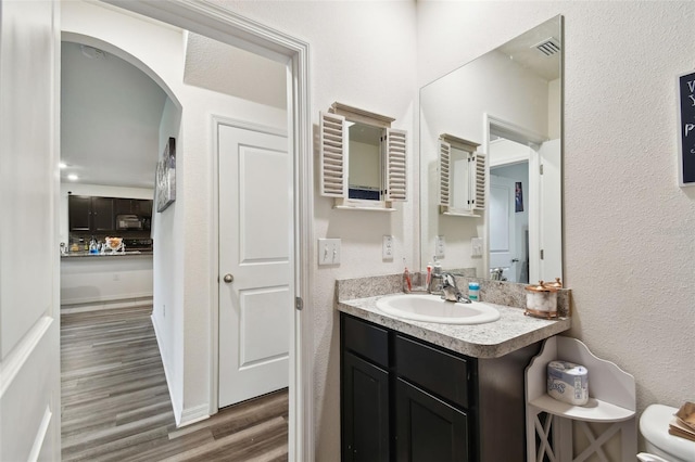 bathroom with visible vents, toilet, wood finished floors, vanity, and a textured wall