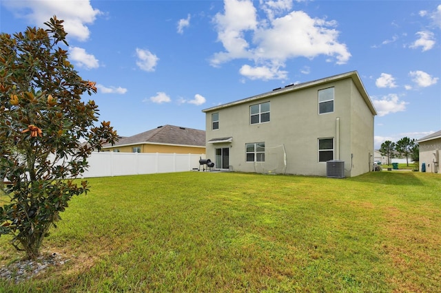 rear view of property with cooling unit, fence, a lawn, and stucco siding