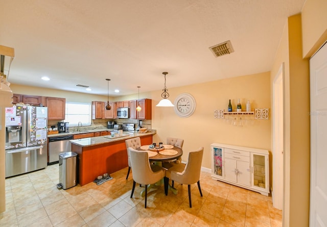 kitchen featuring visible vents, brown cabinets, a peninsula, stainless steel appliances, and a sink