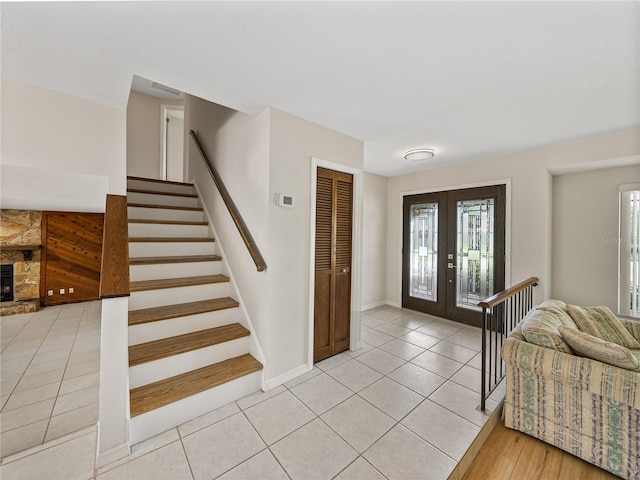 foyer with light hardwood / wood-style flooring, a stone fireplace, and french doors