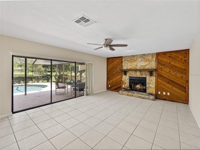 unfurnished living room featuring ceiling fan, a fireplace, wooden walls, and a textured ceiling