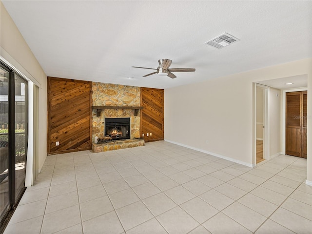 unfurnished living room with light tile patterned flooring, ceiling fan, wood walls, and a fireplace