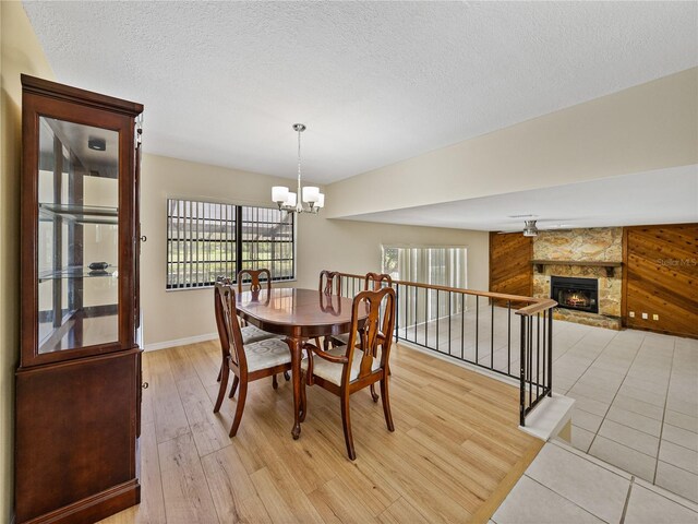 dining room featuring a textured ceiling, light hardwood / wood-style flooring, wood walls, an inviting chandelier, and a stone fireplace