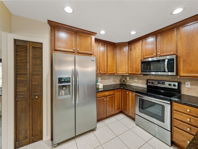 kitchen featuring stainless steel appliances, light tile patterned floors, decorative backsplash, and dark stone counters