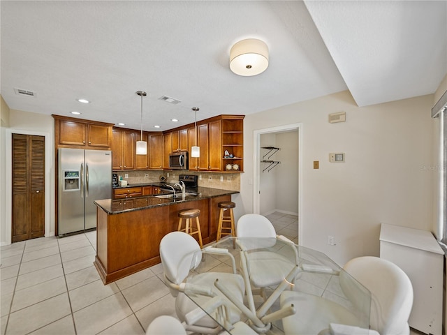 kitchen with decorative light fixtures, light tile patterned floors, tasteful backsplash, stainless steel appliances, and dark stone countertops