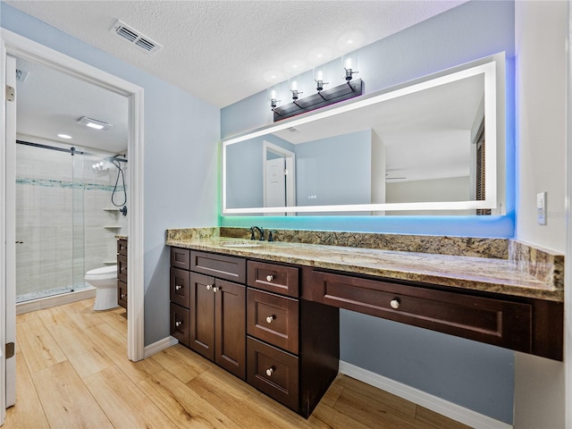 bathroom with an enclosed shower, toilet, wood-type flooring, vanity, and a textured ceiling