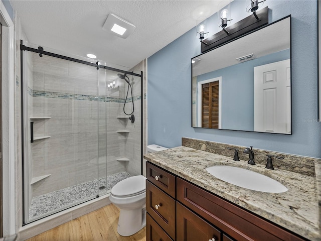 bathroom with toilet, an enclosed shower, vanity, a textured ceiling, and wood-type flooring