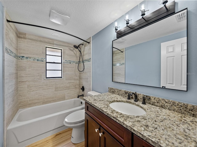 full bathroom featuring a textured ceiling, vanity, wood-type flooring, tiled shower / bath, and toilet