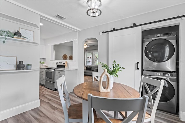 dining space featuring ceiling fan, stacked washer / dryer, a barn door, and hardwood / wood-style flooring