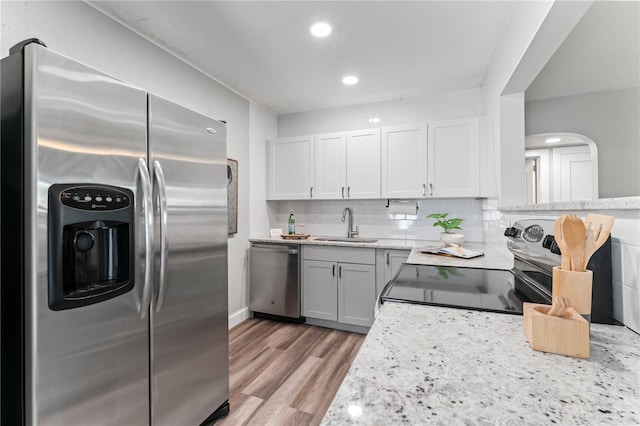 kitchen featuring backsplash, stainless steel appliances, sink, light wood-type flooring, and light stone countertops