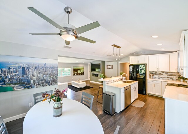 kitchen with vaulted ceiling, dark wood-type flooring, ceiling fan, pendant lighting, and a kitchen island with sink