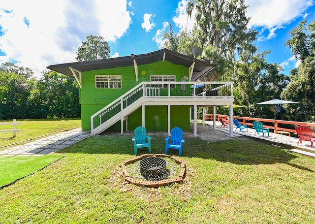 back of house with a fire pit, a wooden deck, a lawn, and a patio