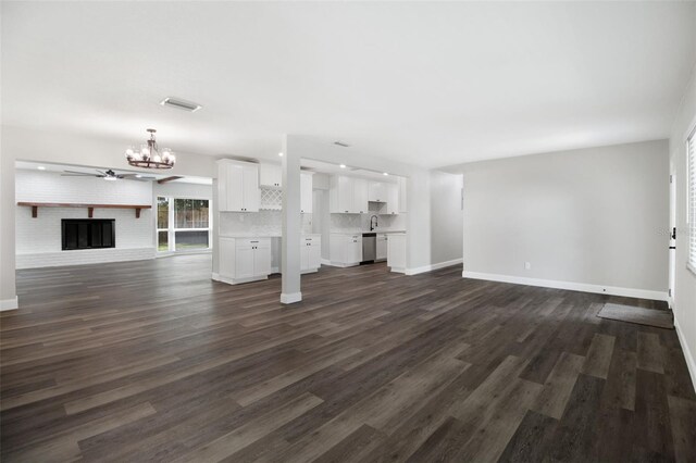 unfurnished living room with dark wood-type flooring, sink, a notable chandelier, and a brick fireplace