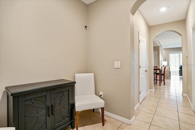 corridor with arched walkways, light tile patterned floors, and baseboards