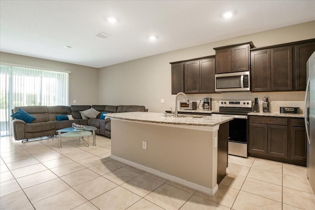 kitchen featuring light tile patterned floors, dark brown cabinetry, stainless steel appliances, a sink, and open floor plan