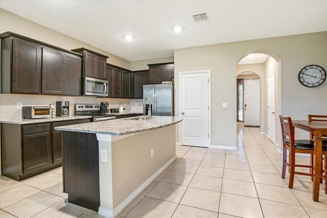 kitchen with arched walkways, light tile patterned floors, visible vents, appliances with stainless steel finishes, and tasteful backsplash