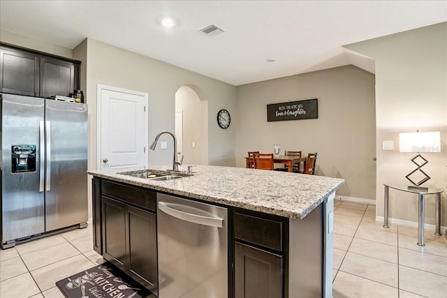 kitchen with light tile patterned floors, arched walkways, appliances with stainless steel finishes, light stone countertops, and a sink