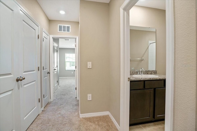 corridor with light carpet, a sink, visible vents, and baseboards