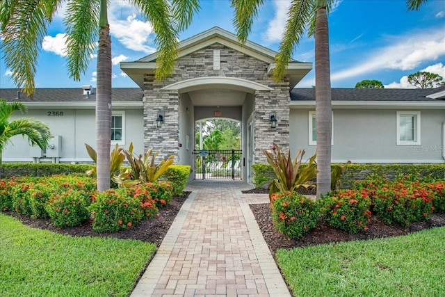 doorway to property featuring a gate, stone siding, and stucco siding