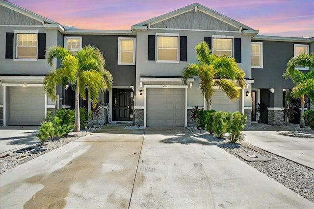 townhome / multi-family property with a garage, concrete driveway, stone siding, and stucco siding