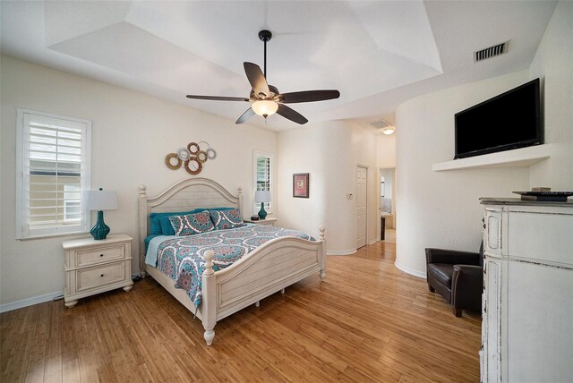 bedroom featuring light wood-type flooring, a tray ceiling, and ceiling fan