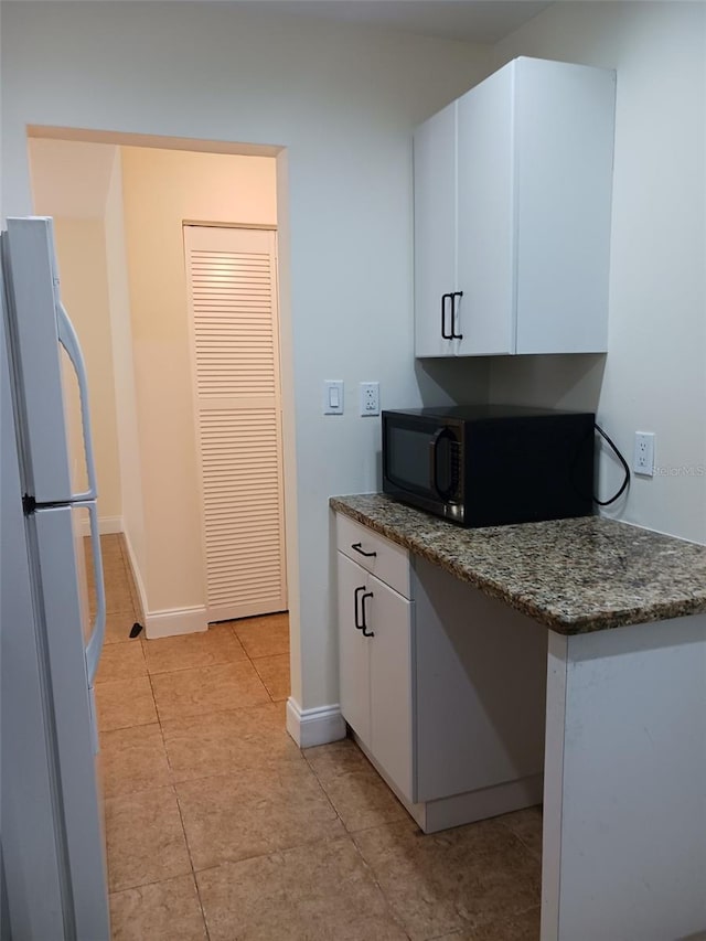 4606 W Gray St Unit 110, Tampa, FL 33609 - kitchen featuring freestanding refrigerator, black microwave, white cabinetry, and light tile patterned flooring