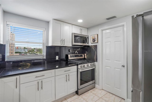 kitchen with appliances with stainless steel finishes, white cabinetry, backsplash, and light tile patterned floors