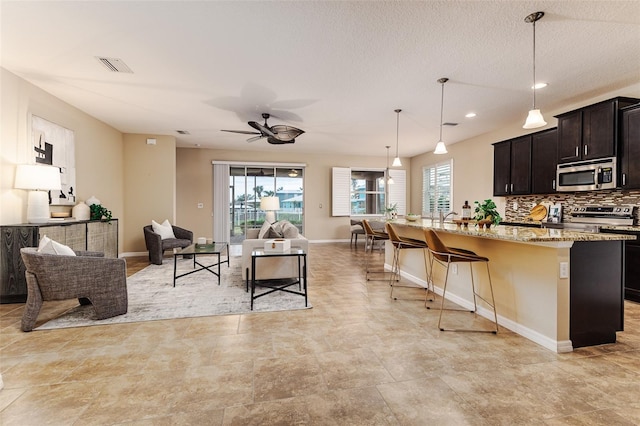 kitchen with a breakfast bar area, appliances with stainless steel finishes, hanging light fixtures, light stone countertops, and a center island with sink