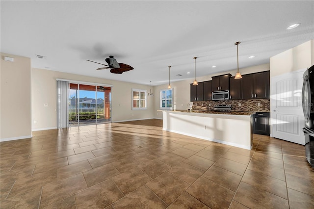 kitchen featuring dark brown cabinetry, decorative light fixtures, a center island with sink, stainless steel appliances, and backsplash