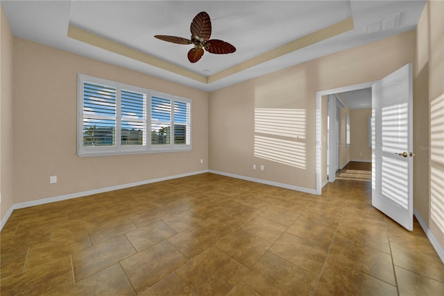 tiled empty room featuring a raised ceiling and ceiling fan