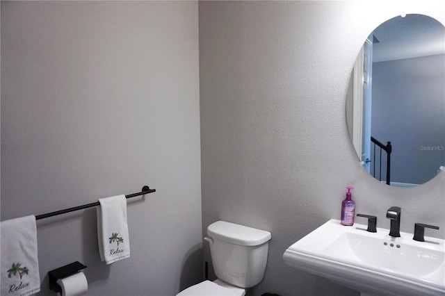 bathroom featuring toilet, a textured wall, and a sink