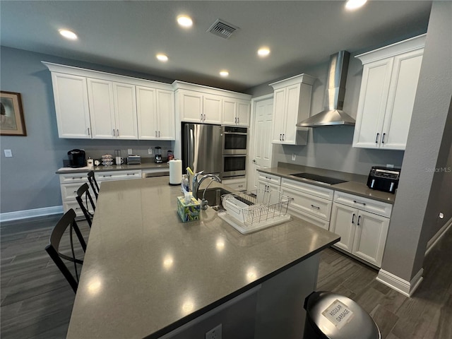 kitchen featuring visible vents, dark wood-type flooring, appliances with stainless steel finishes, white cabinetry, and wall chimney range hood