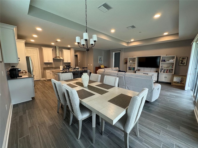 dining space with dark wood finished floors, visible vents, an inviting chandelier, and a tray ceiling