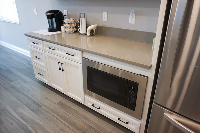 kitchen with dark wood finished floors, appliances with stainless steel finishes, white cabinets, light countertops, and baseboards